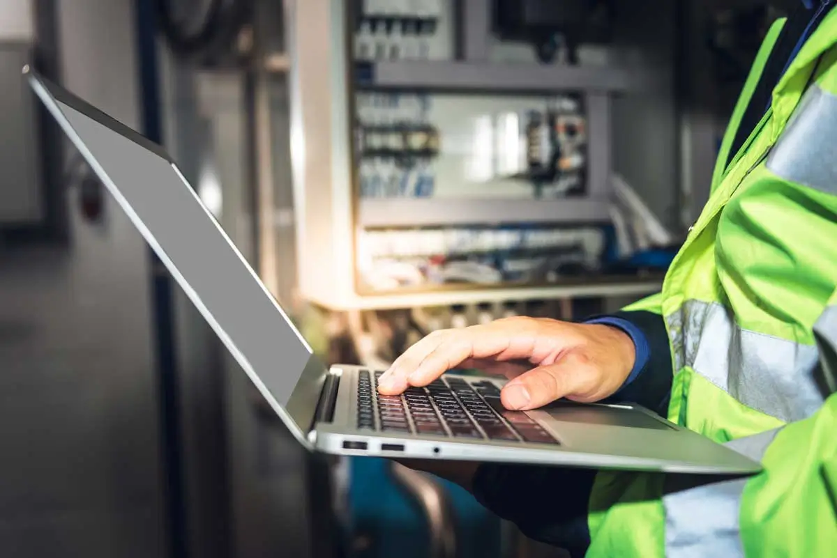 Industrial facility engineer reviewing energy performance indicators on a laptop in a control panel room